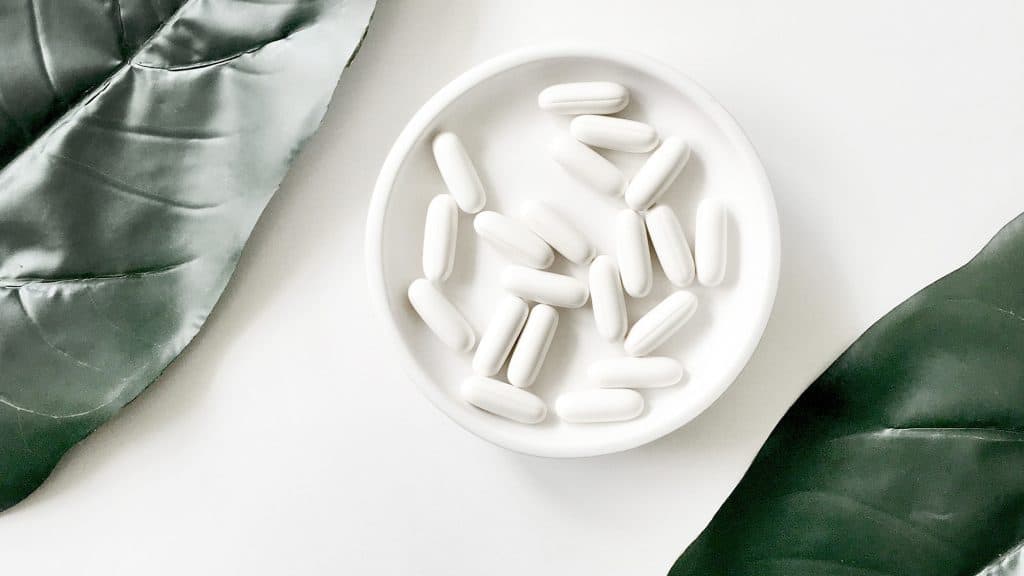 Pills in a ceramic bowl near leaves.