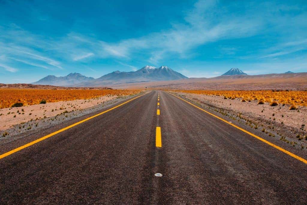 A wide open road out in the desert with mountains in the distance.