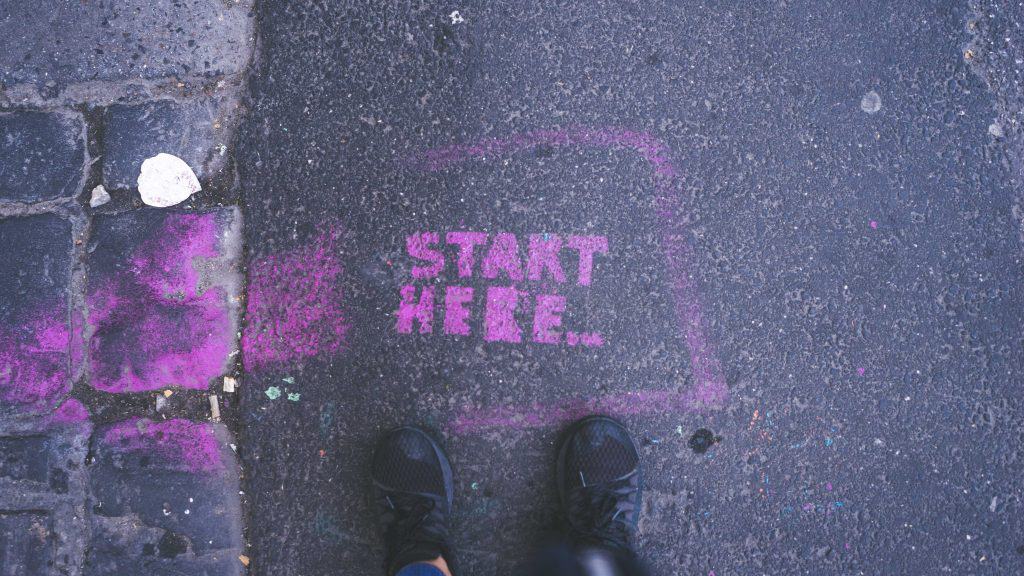Spray painted words on a street, saying "Start here"