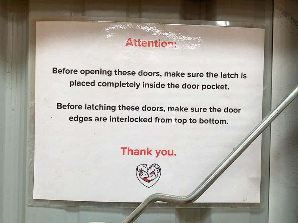 Laminated sign at Luvin Arms Animal Sanctuary. It reads "Attention: Before opening these doors, make sure the latch is placed completely inside the door pocket. Before latching these doors, make sure the door edges are interlocked from top to bottom. Thank You."