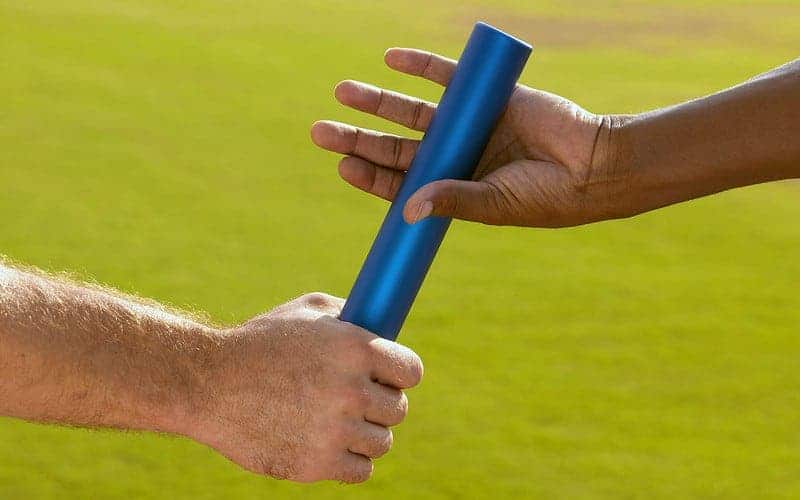 Two people pass off a baton from one to the other on a run.