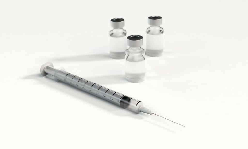 A syringe next to three vials.