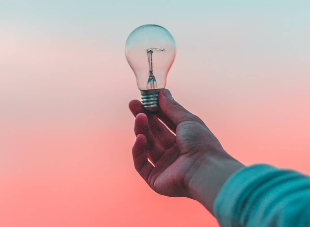 A lightbulb being held up to a pleasant color gradient