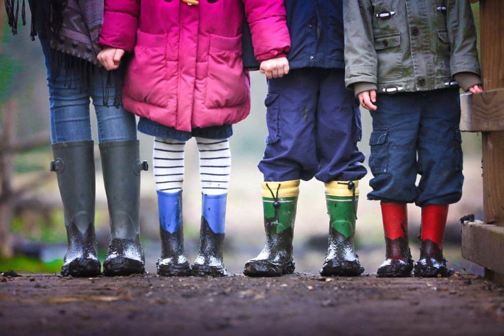 One adult and three children are holding hands and wearing muddy boots. 