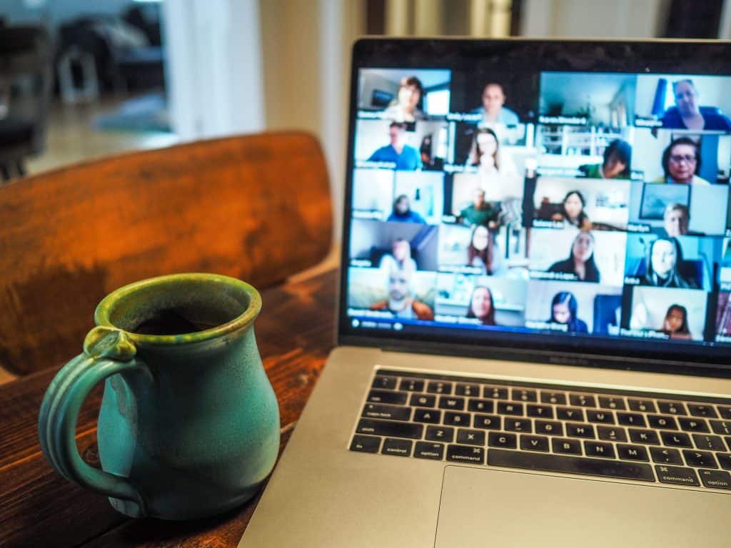 Close-up of a large teal coffee cup is next to a laptop with several people on the screen in separate boxes.