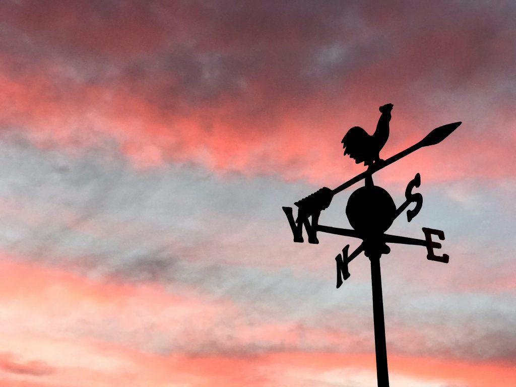Pink and purple sky in the background. To the right of the foreground is a weather vane with a rooster on top.