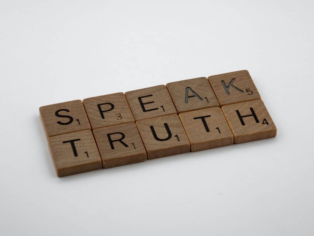 A white backdrop with light brown Scrabble letters on top. The letters spell "Speak Truth".