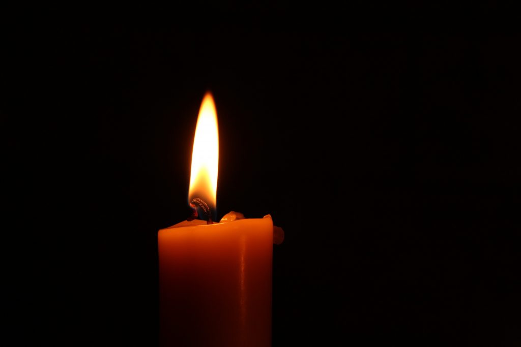 A black backdrop with a red candle in the middle. The candle is lit.