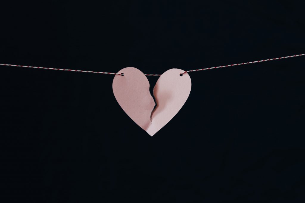A black backdrop with a piece of string hanging across holding a small broken pink heart in the middle.