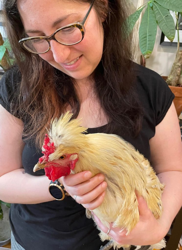 A woman with glasses holds a white rooster.