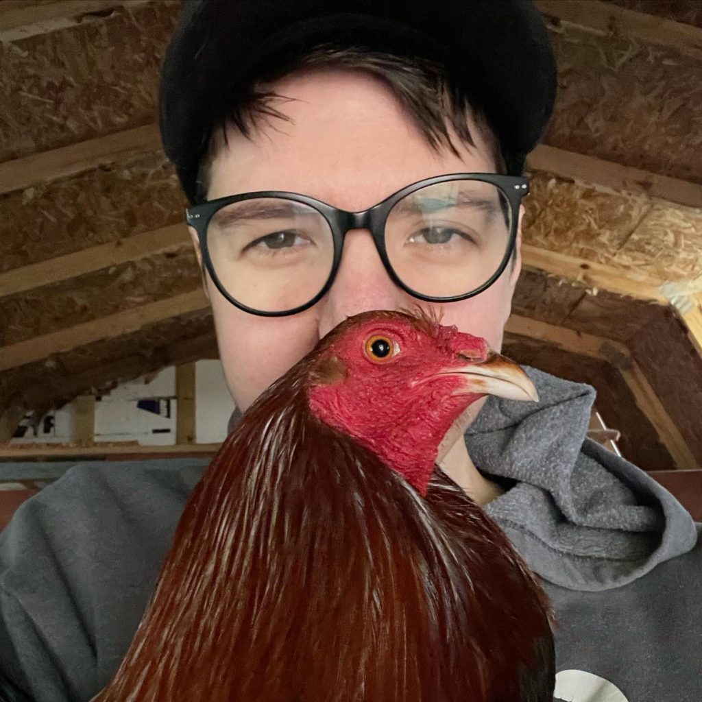 A person with glasses holds an ex fighting rooster to their face in affection.