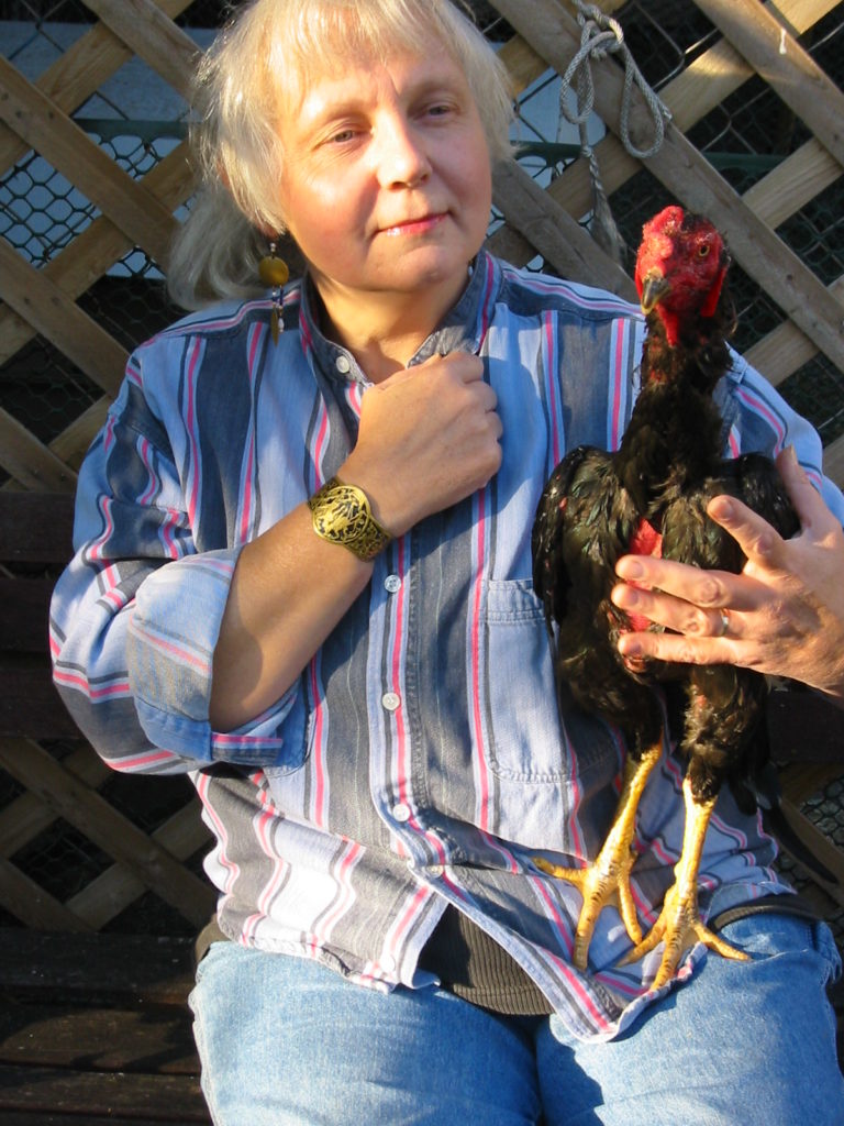 A woman holds an ex fighting rooster, and holds her fist over her heart.