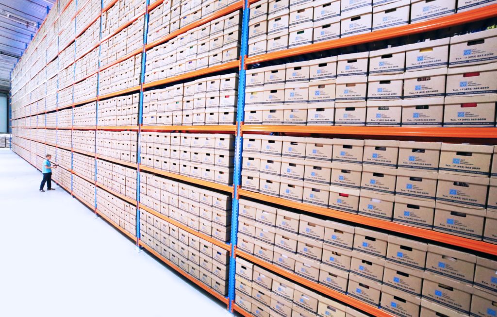 An image of a warehouse of organized record storage boxes with a person searching for a box.