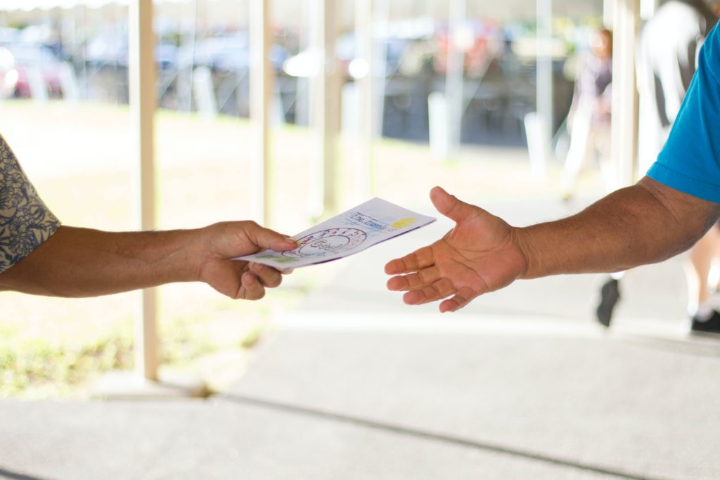 Photograph of someone handing another person a brochure. Only their arms are visible.