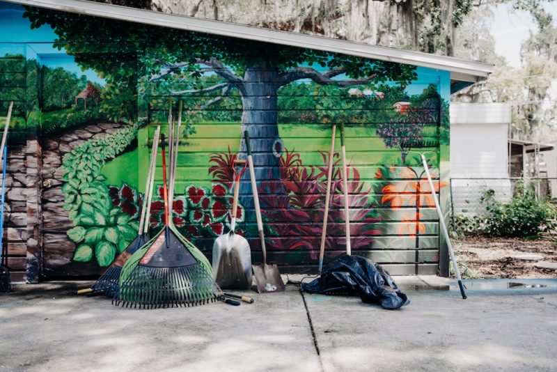 rakes and shovels lean against a mural-painted wall