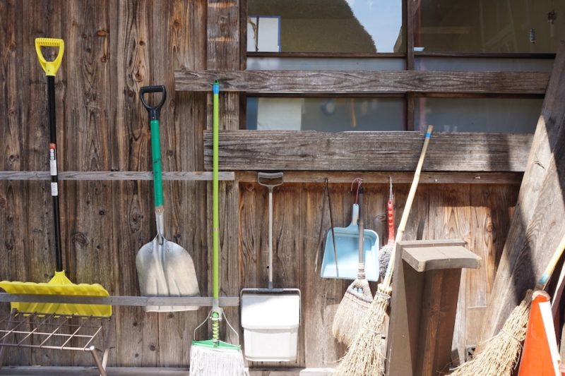 shovels, brooms, and other cleaning supplies hang from a wood wall
