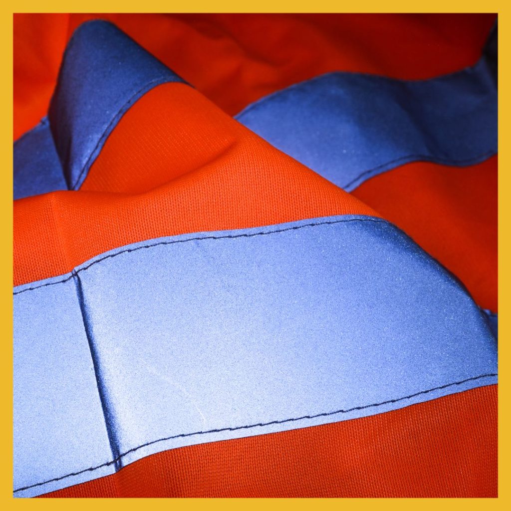 This image shows a close up of a bright orange safety vest, that has reflective tape sewn onto it.