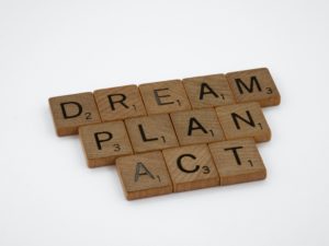 An image of three words stacked and spelled out by Scrabble blocks. The first reads: Dream. The second reads: Plan. The third reads: Act.