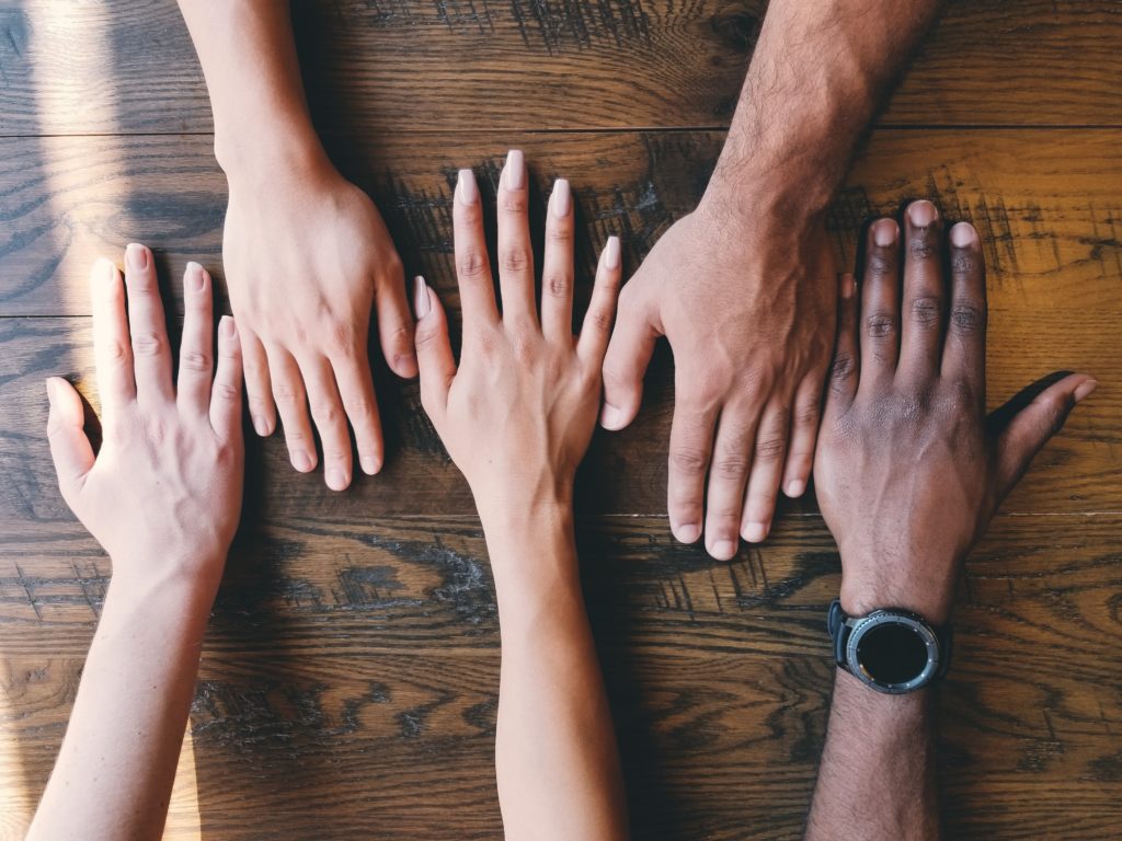 An image of five hands reaching towards each other across a table. 