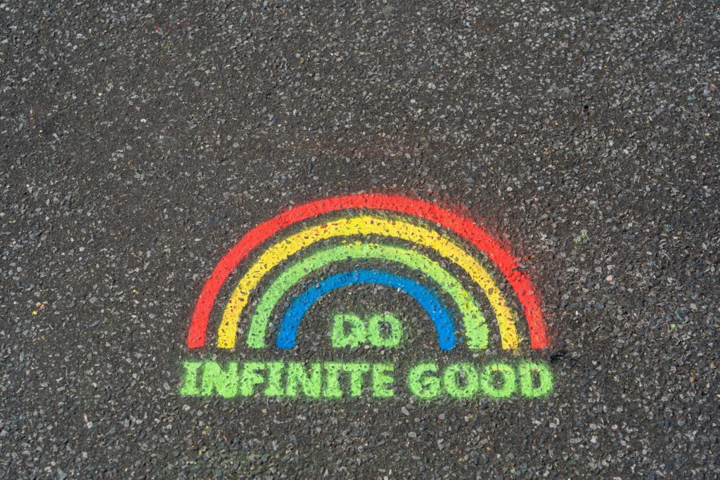 An image of a rainbow spray painted on concrete. Underneath rainbow are the words "Do infinite good."
