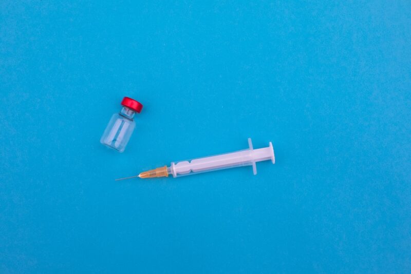 a small medicine vial and syringe sit against a blue background