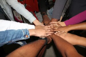 An image of eight hands reaching towards each other and clasping together at the center.