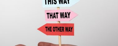 Small signpost in a person's hand that reads "this way, that way, the other way".