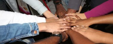 An image of eight hands reaching towards each other and clasping together at the center.