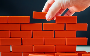 A hand places red toy bricks on top of one another, building a wall.