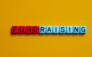 Red and light blue square beads spell out "FUNDRAISING" on a mustard yellow background.