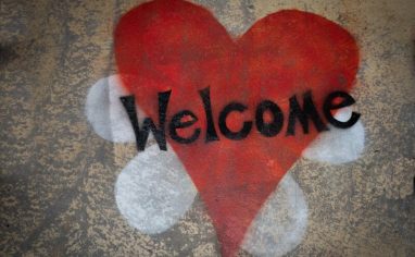A photograph of a spray painted red heart on concrete. The word welcome is spray painted in black on top of the heart.