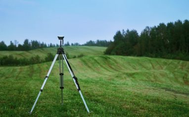 An image of surveying equipment placed on a green field, with forest in the area.